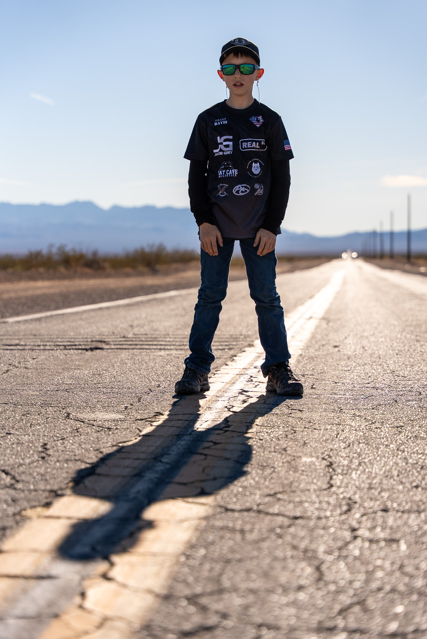 Boy flexing, full body standing on road with mountains